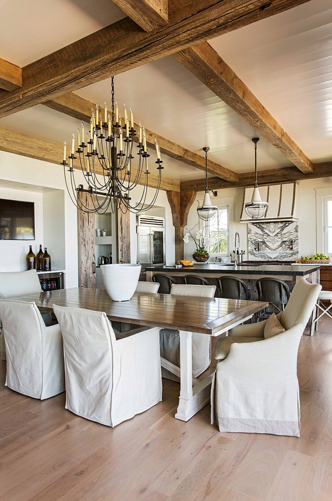 Rustic coastal dining room. This rustic coastal dining room have a casual elegant feel. Relaxed slipcovered chairs add some comfort to this space. Lighting is Visual Comfort TOB5206AI Thomas O'Brien Erika Three-Tier Chandelier in Aged Iron #rustcidiningroom #coastasldiningroom #rusticcoastal #diningroom #lighting Herlong & Associates Architects + Interiors