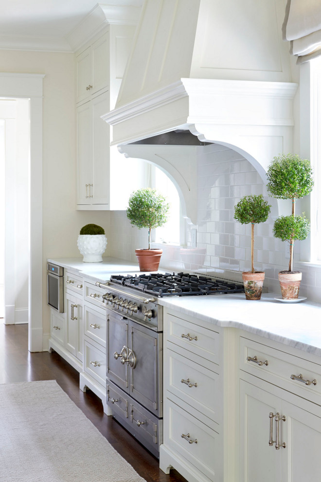  White Kitchen with Topiaries. Exquisite kitchen features a white paneled kitchen hood with corbels, flanked by windows and topiaries, suspended over a French range. white-kitchen-with-topiaries #WhiteKitchen #Topiaries Sarah Bartholomew Design