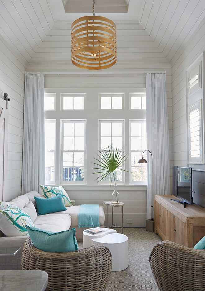 Apartment shiplap interior. This small apartment features shiplap walls and shiplap ceiling. The small living room features a taupe sectional lined with turquoise blue pillows facing a low wood tv cabinet. A gold striped drum pendant hangs from a tray shiplap ceiling while a pair of wicker pod chair provides additional seating. #shiplap #apartment apartment-shiplap-interiors