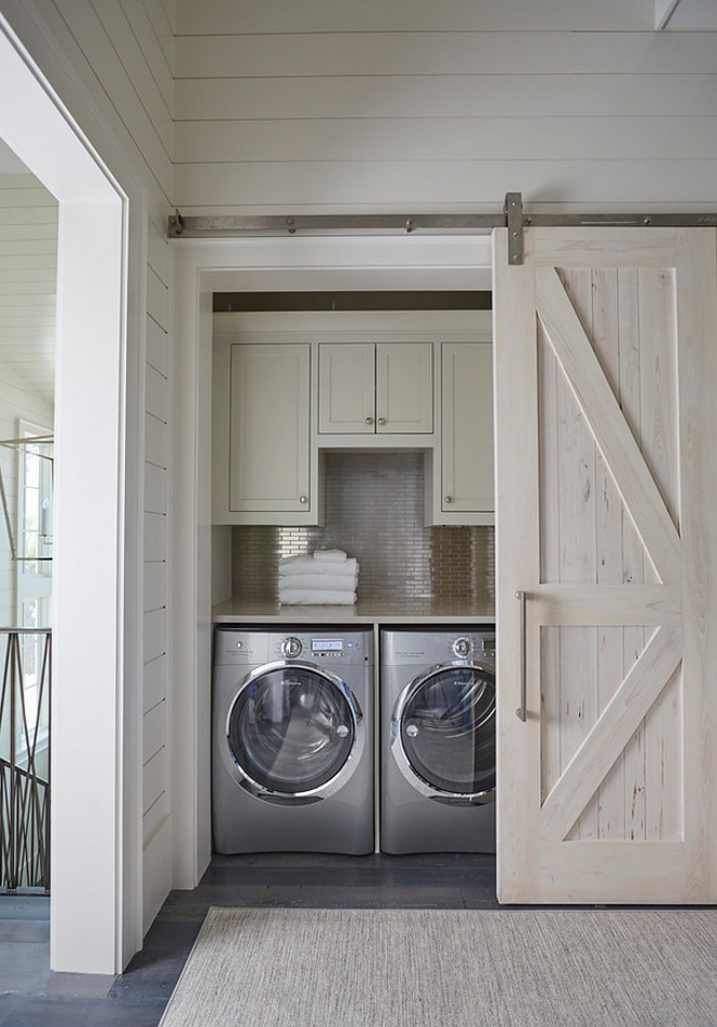 Barn door closet laundry room. Closet Laundry Room with Pecky Cypress Barn Door on Rails. A pecky cypress barn door on rails opens to a hallway laundry room filled with light gray shaker cabinets suspended over a stainless steel mini brick tile backsplash and an enclosed washer and dryer. Washer and dryer are Electrolux. barn-door-closet-laundry-room #barndoor #closetlaundryroom #laundryroom #closet #barndoorideas #closetbarndoor