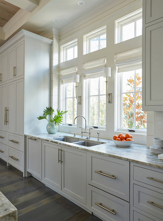  Row of Windows Over Kitchen Sink. Kitchen Windows. The light gray kitchen cabinets are adorned with extra long satin nickel pulls. A stainless steel dual kitchen sink stands under a row of windows dressed in white roman shades illuminated by Ruhlmann Single Sconces. #kitchenwindow #romanshades #whiteromanshades #kitchenwindows #kitchen #window kitchen-window Geoff Chick & Associates