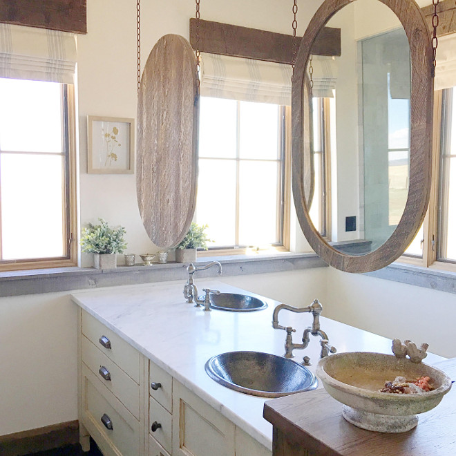 Bathroom. Rustic Bathroom Design. Painted and glazed alder cabinets make up this double sided vanity, which ends in a custom distressed oak cabinet fashioned to look like furniture. Mirrors hung by antique chains allow light to bounce through the space, and the homeowners to interact with each other. Master bathroom Hanging mirrors: Oval mirrors with Montana wood siding. Master Bath Countertops: Carrera Marble. Paint color is Benjamin Moore OC-130. Window Treatment: Pottery Barn. #bathroom #rusticbathroom Home Bunch's Beautiful Homes of Instagram @birdie_farm