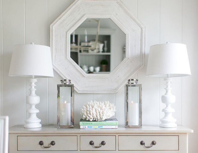 Neutral dining room console table decor. This beautifully decorated dining room features vertical shiplap paneling, a whitewashed octagon mirror above an ivory console table accented with dark nickel vintage pulls and topped with white table lamps flanking nickel candle lanterns. Neutral dining room console table decor ideas. Coastal and Neutral dining room console table decor AGK Design Studio. Ryan Garvin Photography.