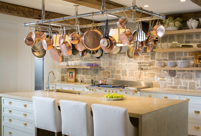 Rustic white kitchen. Rustic white kitchen with concrete waterfall island countertop, custom pot rack, open shelves, rustic reclaimed beams, open shelves and fieldstone backsplash wall. Bayview Builders LLC