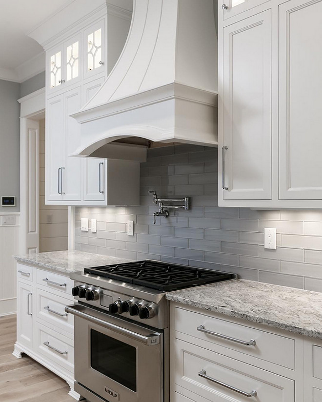 Grey backsplash. White Kitchen with Grey Subway Tile. Inset cabinets, oversized chrome handles, lighted upper cabinets, curved range hood and a wolf range and just a couple key elements for a great kitchen. White Kitchen with Grey Subway Backsplash Tile. #GreyBacksplash #WhiteKitchen #GreySubwaytile GreySubwayBacksplashTile #GreyBacksplashTile Artisan Signature Homes via Instagram.