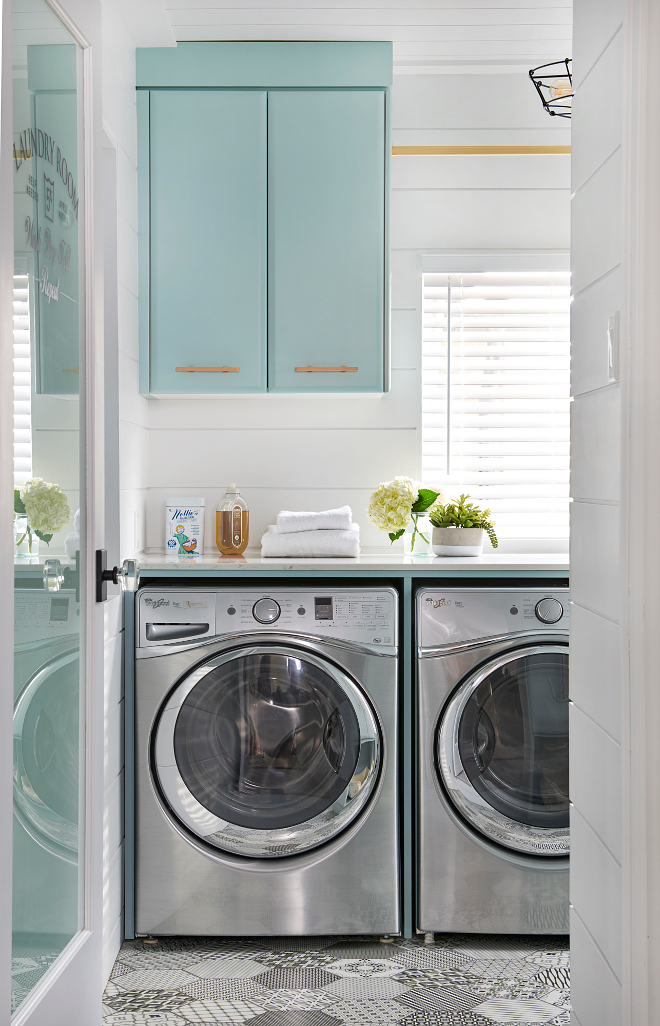 Laundry room with turquoise cabinets, cement tile flooring and brass hardware. This dream laundry room features black and white hex cement floor tiles and a silver front loading washer and dryer enclosed beneath a white quartz countertop. The laundry room walls are paneled with horizontal shiplap. #Laundryroom #turquoisecabinet #Turquoise #brasshardware #hardware Soda Pop Design Inc.