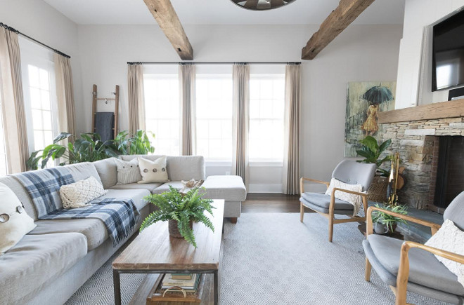 Neutral living room features light grey sofa sectional, a pair of mid-century chairs by stacked stone fireplace, natural linen draperies and reclaimed wood beams. #Neutrallivingroom #lightgreysofa #lightgreysectional #midcenturychairs #stackedstonefireplace #naturallinendraperies #reclaimedwoodbeams Beautiful Homes of Instagram @greensprucedesigns