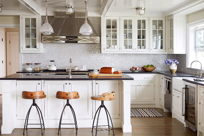 White kitchen painted in Benjamin Moore Decorators White. This Hamptons-style white kitchen also features shaker-style cabinetry, olive knuckle hinges, glazed white terracotta backsplash, custom hardware made from a mold of an antique pull and a gorgeous custom stainless steel range hood. Wall paint color is White Drifts by Benjamin Moore. Trim, ceiling and cabinets are Benjamin Moore Decorator's White. Benjamin Moore Decorators White #BenjaminMooreDecoratorsWhite Andrew Howard Interior Design