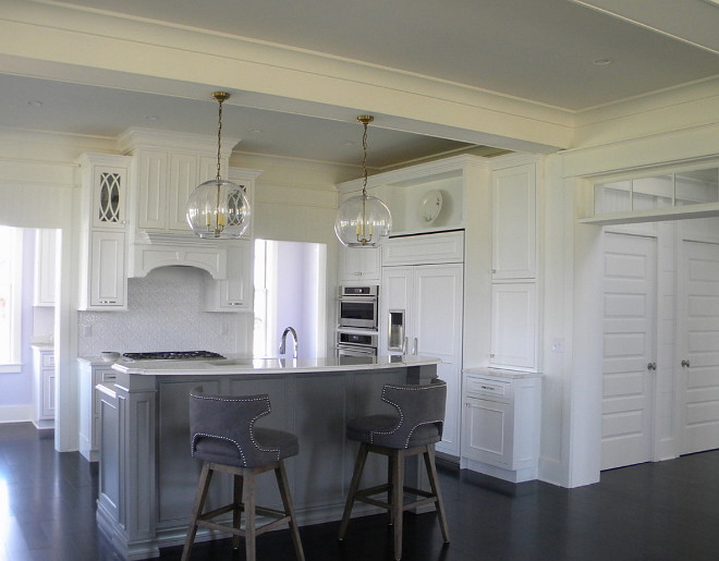 White kitchen with dark hardwood floors, globe lights, trabsom windows and open to living room. Our Town Plans