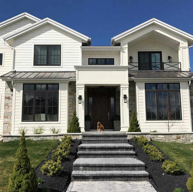 Modern Farmhouse Style Exterior. Modern Farmhouse Style Exterior with white siding, neutral natural stone, Black Paned Windows, custom railing and metal roof. #ModernFarmhouse #ModernFarmhouseStyle #ModernFarmhouseStyleExterior #ModernFarmhouseExterior #FarmhouseExterior #whitesiding #naturalstone #stoneexterior #BlackPanedWindows #railing #metalroof Caitilin Creer Interiors