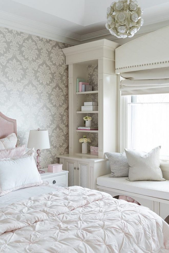 Bedroom window seat flanked by bookshelves. A built-in window seat with storage stands under a picture window dressed in a white curved cornice box finished with silver nailhead trim flanked by tall built-in bookcases Tara Fingold Interiors