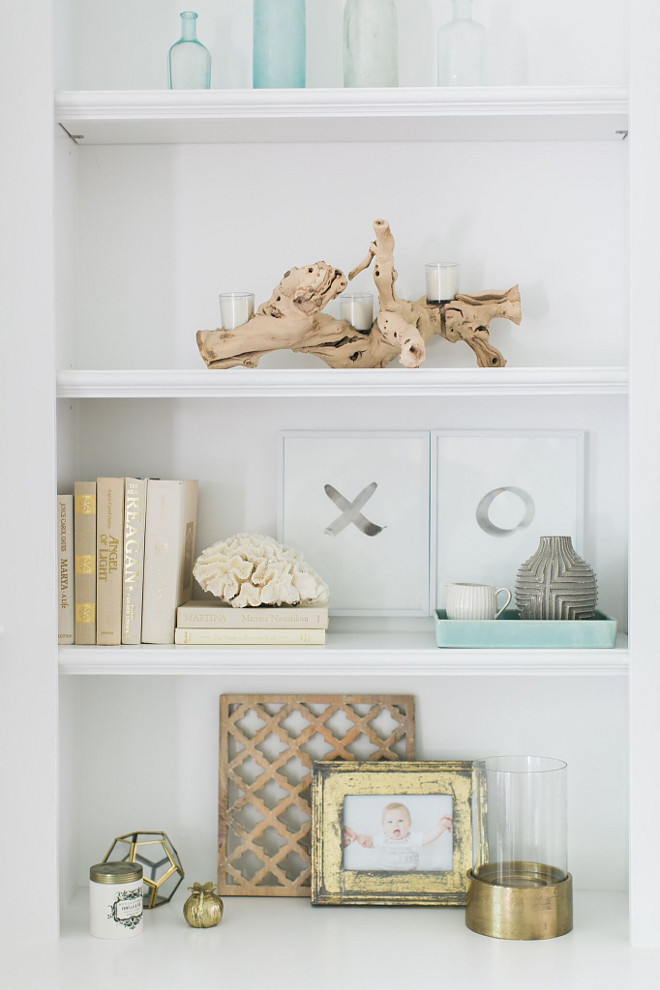 Coastal Bookshelf Decor. Coastal Neutral Bookshelf Decor. Driftwood, photo frames, vintage bottles, linen covered books and a touch of brass accessories. Shelves paint color is Benjamin Moore Decorator’s White. Coastal Bookshelf Decor. Coastal Neutral Bookshelf Decor #Coastal #BookshelfDecor #BookshelfDecor #NeutralBookshelfDecor #neutralBookshelf #Bookshelf #Decor Home Bunch Beautiful Homes of Instagram @finding__lovely