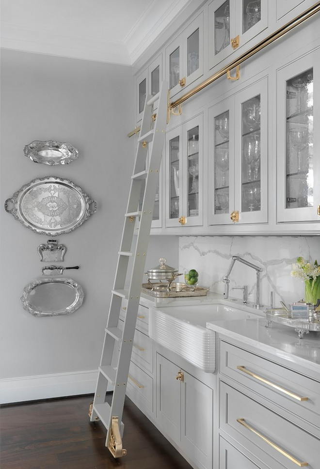 Grey Cabinet with Brass hardware. The butler's pantry features grey cabinet, removable cabinet ladder and brass hardware. Sink is Kohler, Whitehaven in White. Grey kitchen cabinet with brass hardware and removable cabinet ladder #GreyCabinet #Brasshardware #Greykitchencabinet #Greycabinetbrass #hardware #cabinetladder Mitchell Wall Architecture & Design