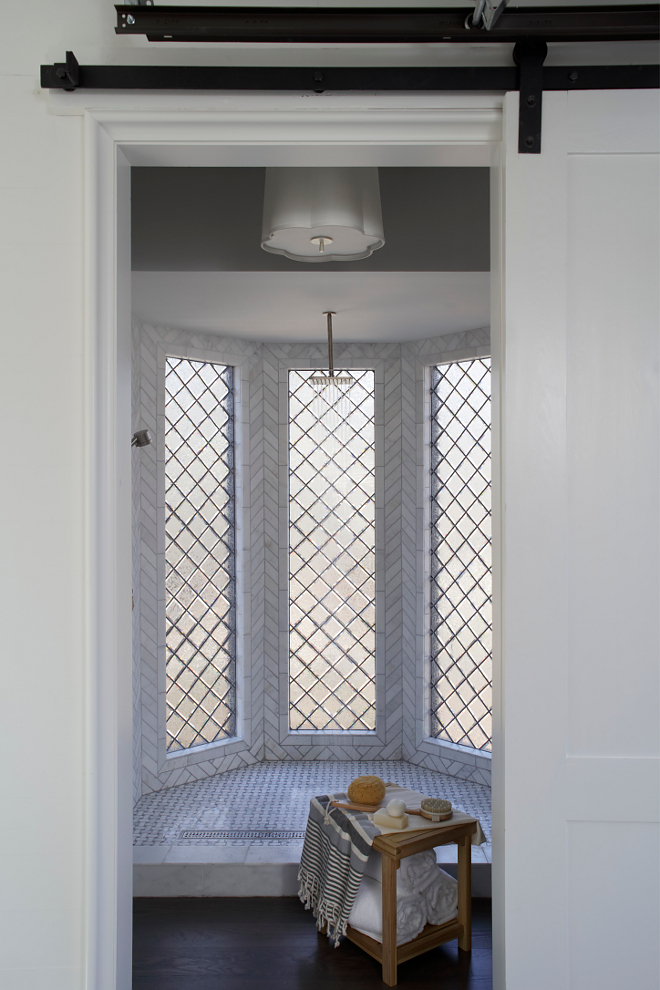 Bathroom Barn Door. Custom barn door separates bedroom and bath. Walk in Shower with Cararra marble tiles installed in a herringbone pattern on the walls and Lead glass tiles #bathroom #barndoor #walkinshower #shower #showerwindow #herringbonetile Christopher Architecture & Interiors. Joanna Goodman.