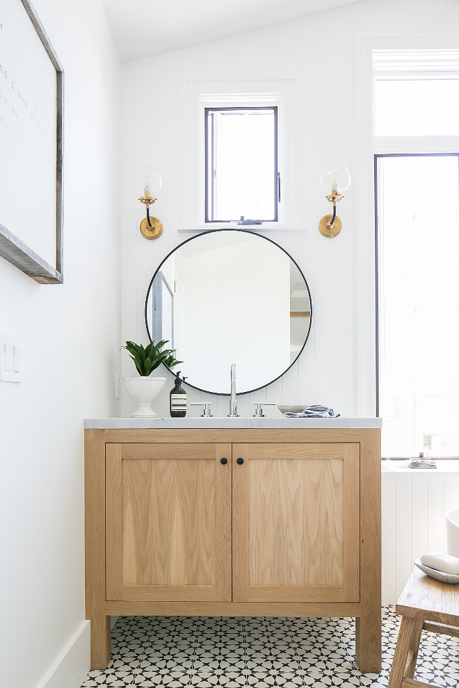 Farmhouse bathroom with black and white cement tile, white oak vanity, round metal mirror and brass glass sconces