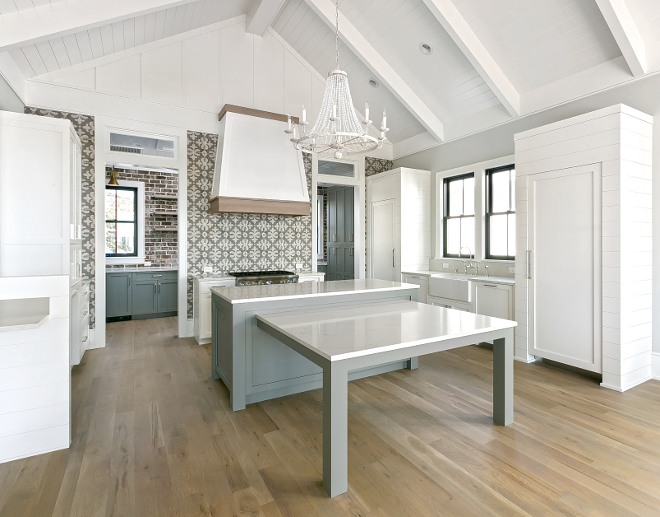 Transitional white and grey kitchen with vaulted shiplap ceiling, shiplap cabinet paneling, cement tile backsplash, white oak hardwood floors and kitchen island with attached table