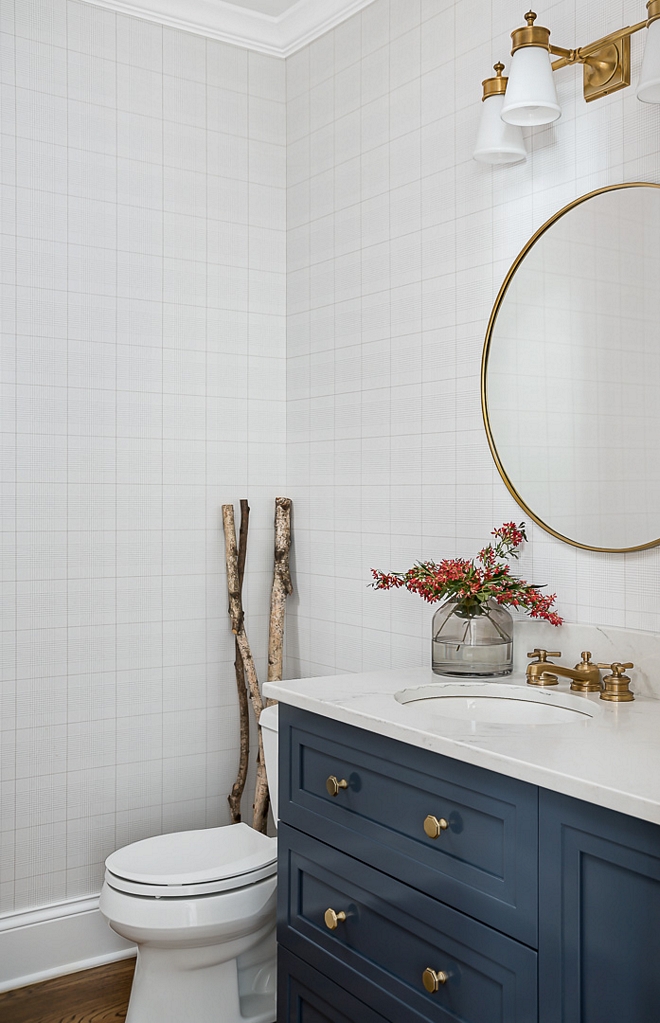 Bathroom with plaid wallpaper Zodiaq in London Sky quartz countertop round brass mirror brass pull hardware and navy blue cabinet