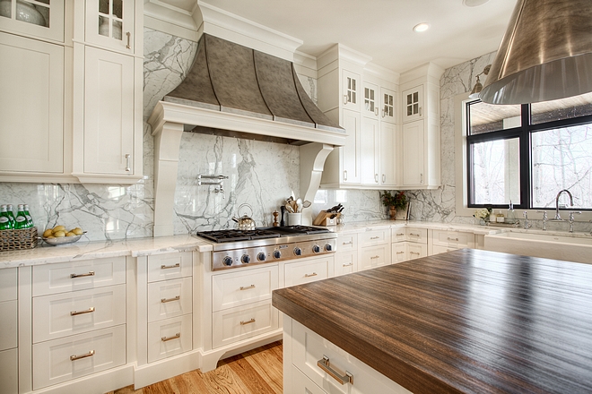 Perimeter countertop and slab backsplash is Statuario marble Kitchen Custom stainless steel hood and cabinetry is accented by the solid slab marble back splash and countertops