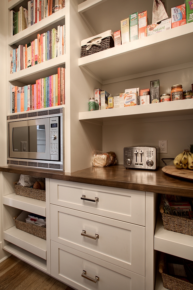 Pantry features pull out baskets, ample storage, and built-in microwave with cookbook storage above #pantry #cookingbooks