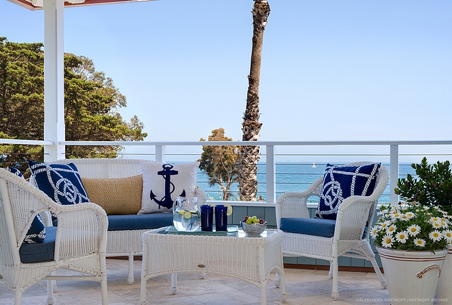 Coastal patio with outdoor white wicker set of sofa, chairs and coffee table Coastal Blue and white outdoor pillows sources on Home Bunch #coastalpatio #whitewicker #outdoorwickerset #outdoorpillows #coastalpillows