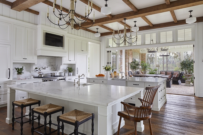 Kitchen The spacious kitchen has two large marble-topped islands, perfect for entertaining. A sixteen foot bifold door opens to the screened porch, allowing the homeowners to take advantage of the breeze while also creating a seamless transition between inside and out #kitchen #whitekitchen #kitchendoor #patiodoor #kitchens