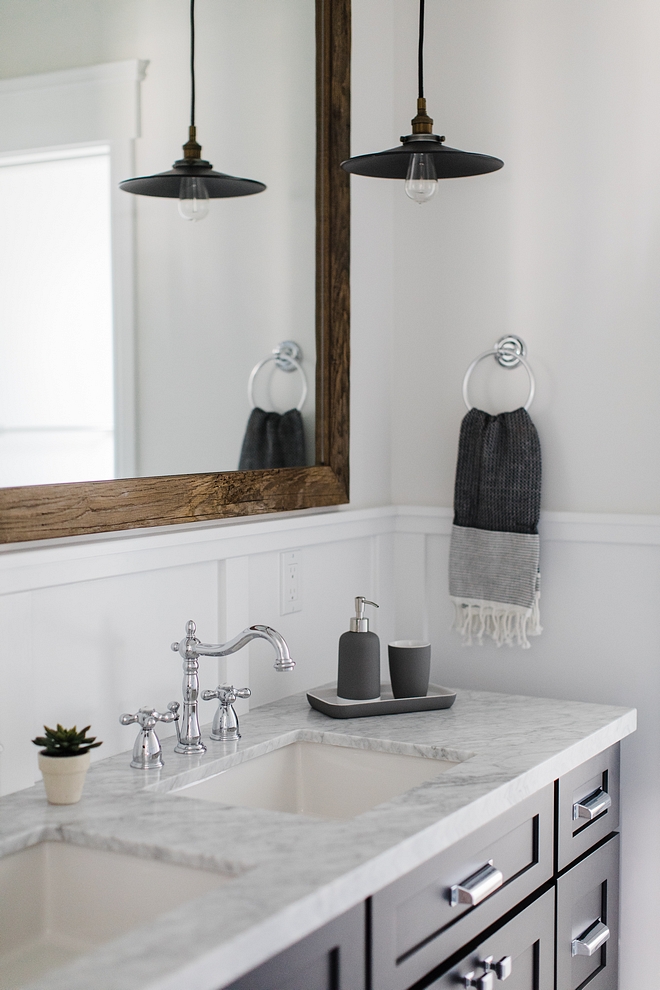 Bathroom features a dark charcoal cabinet with white marble top, double sinks and a large barnwood mirror Sources on Home Bunch #bathroom