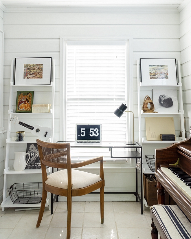 Small sunroom used as a home office with bookcases flanking a window and a metal and glass desk with vintage cane back chair