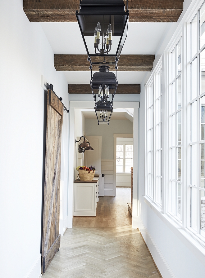 Hallway This charming hallway, painted Sherwin Williams SW7008 Alabaster, features herringbone hardwood flooring, reclaimed barn door and ceiling beams #halway #SherwinWilliamsSW7008Alabaster #herringboneflooring #hardwoodflooring #reclaimedbarndoor #reclaimedwood #beams