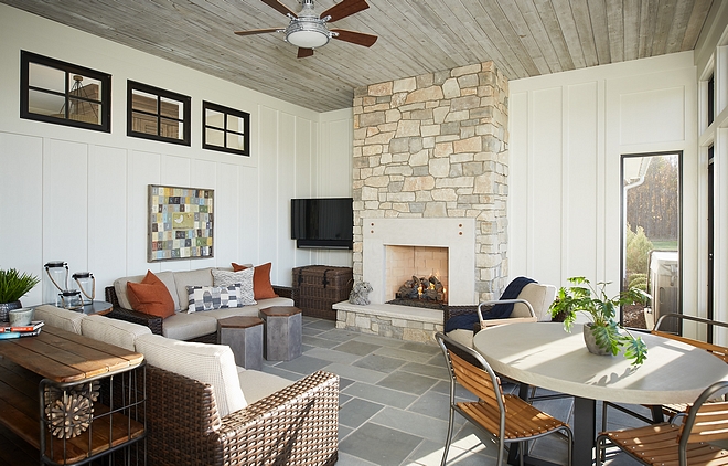 The screened porch features a stone fireplace, Bluestone floor tile, board and batten siding and reclaimed wood shiplap ceiling