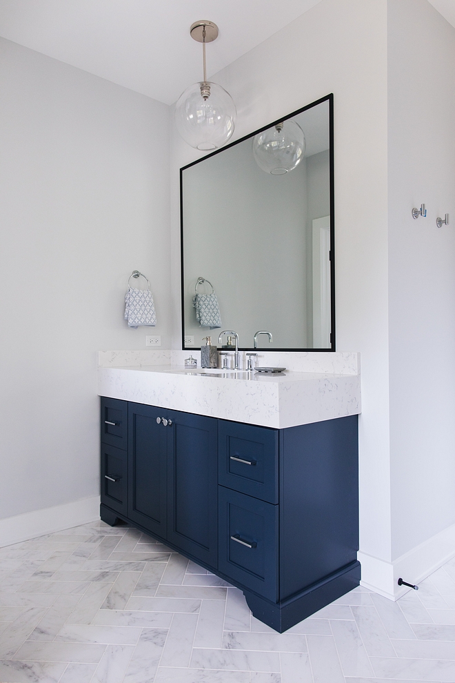 Bathroom with light grey walls painted in Sherwin Williams Site White 7070, navy blue vanities with chunky marble countertop and herringnone floor tile #bathroom #navybluevanity #chunkycountertop