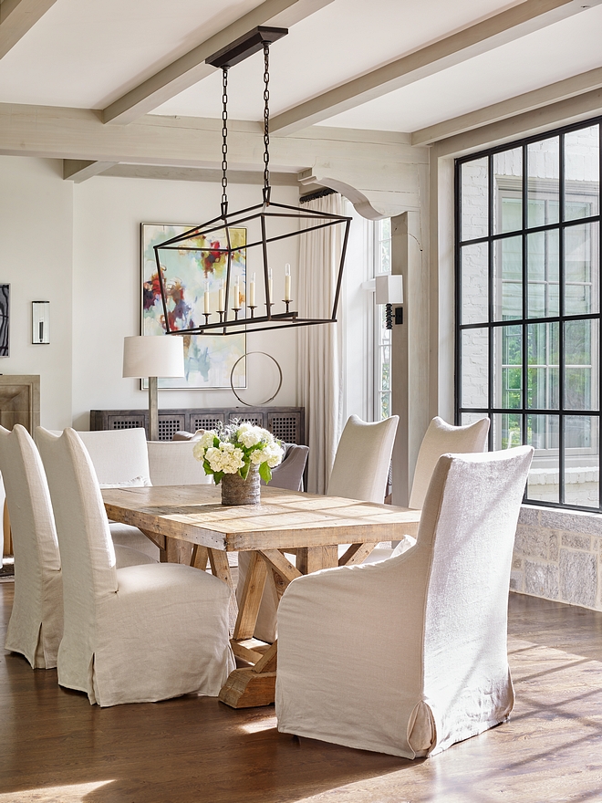 Dining Room featuring greywashed ceiling beams, corbels, Salvaged Wood trestle dining Table and black steel casement window Neutral Dining Room featuring greywashed ceiling beams and black steel casement window slipcovered dining chairs and a farmhouse dining table #DiningRoom #greywashedbeams #ceilingbeams #ceilingcorbel #corbel #blacksteelcasementwindow #blackcasementwindow #blacksteewindow #casementwindow #blackwindow #SalvagedWood #trestlediningTable