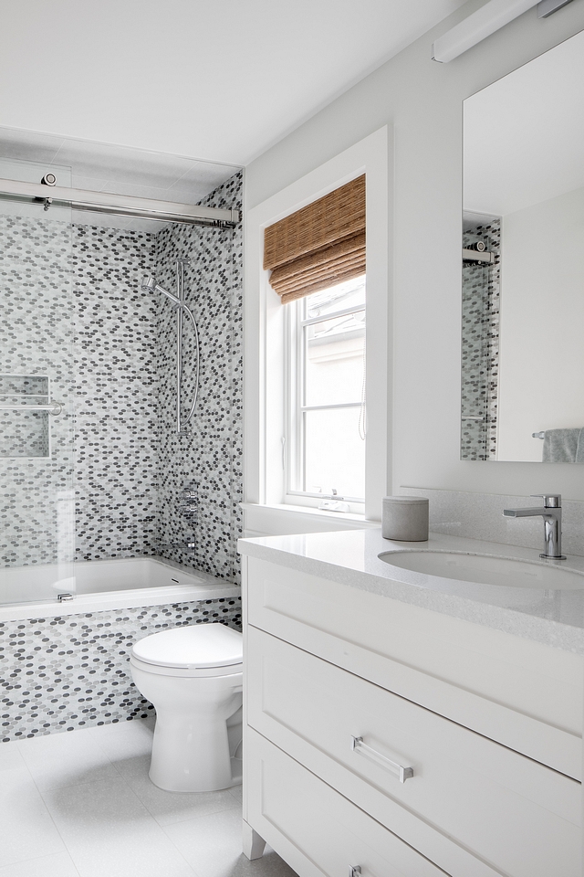 Bathroom This bathroom features a custom white vanity, painted in Benjamin Moore Atrium White and oval mosaic tile in shower and tub front #bathroom