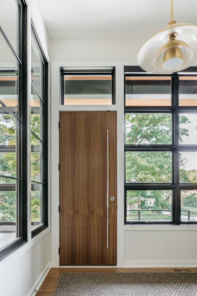 A sleek custom Walnut front door in clear stain opens into a Foyer surrounded by black framed windows