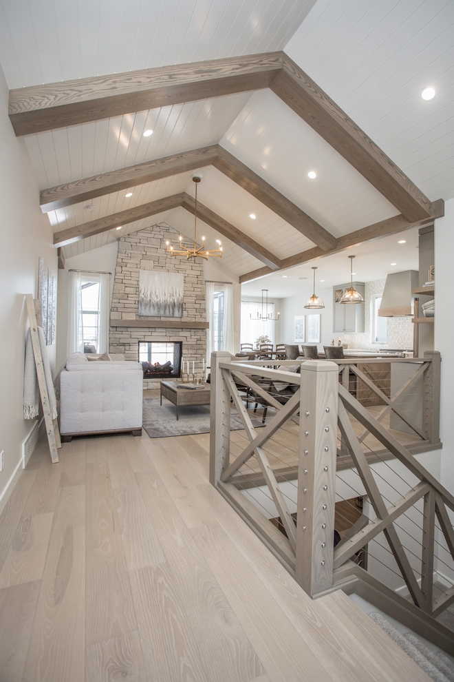 A vaulted ceiling with wood beams and shiplap centered on the double sided stone clad fireplace make this living room the heart of the home #vaultedceiling #woodbeamsshiplapceiling #woodbeams #shiplap #Bemans #doublesidedfireplace #stonefireplace #stonecladfireplace Farmhousestaircase #Xrailing #cablerailing #livingroom