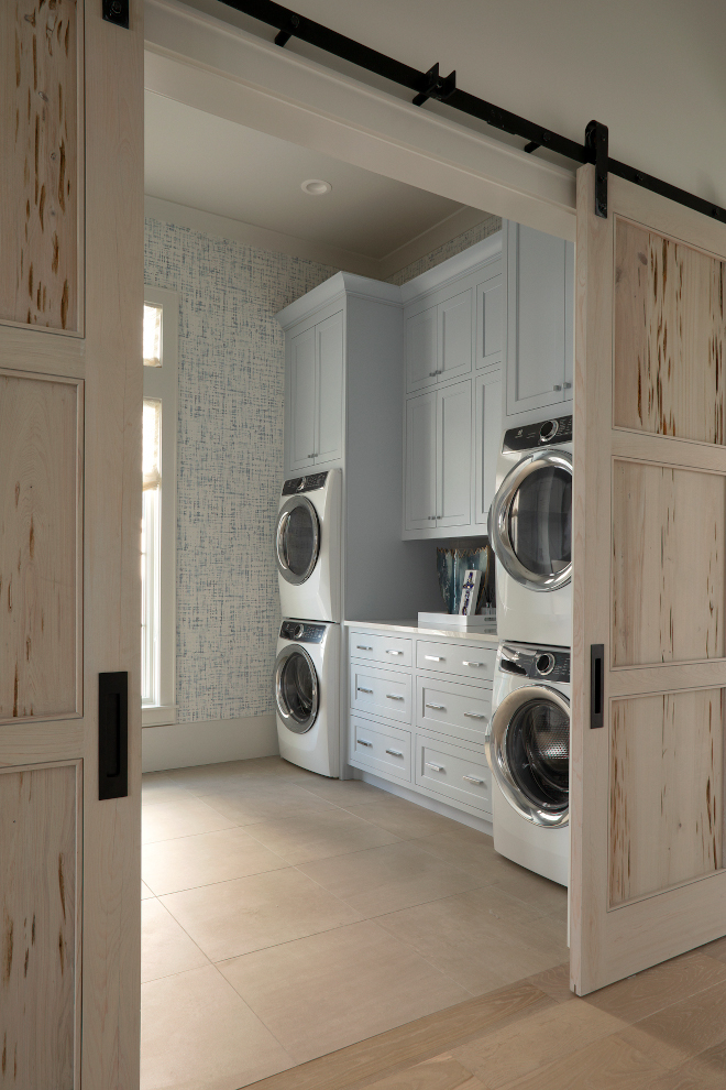 Featuring Pecky Cypress barn doors, blue gray cabinets and two sets of stacked washer and dryers, this beach house Laundry Room would certainly make our lives a little easier #laundryroom #beachouse #twosetswasherdryer #stackedwasheranddryers #barndoor #peckycypress