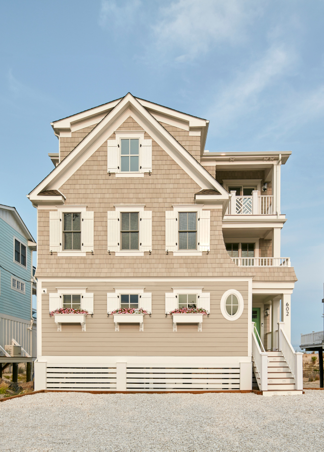 Beach House Outside the home the unique exterior design is accentuated by Sherwin Williams Worldly Gray siding with a bright front door and charming window boxes #BeachHouse #home #uniqueexterior #exterior #exteriordesign #SherwinWilliamsWorldlyGray #siding #frontdoor #windowboxes