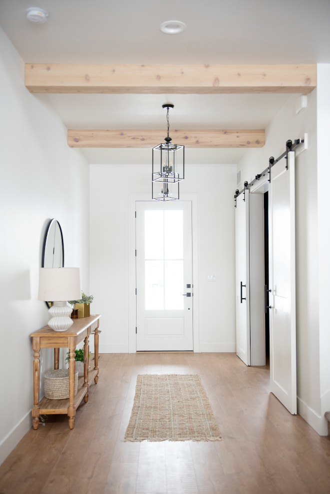The front door opens to a spacious Foyer with white walls and ceiling beams On the right a pair of custom barn doors open to a quiet Home Office #frontdoor #Foyer #whitewalls #ceilingbeams #beams #barndoors #HomeOffice