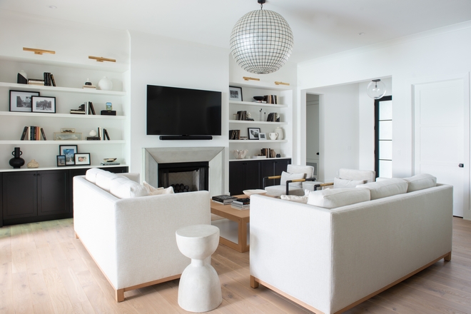 The formal living room is designed with custom built cabinetry, surrounding a fireplace with black cannon balls, and topped with a pearlescent shell pendant to illuminate the space. This space, as seen throughout the home, welcomes contrast from the lower black cabinets, playing off the white oak wood