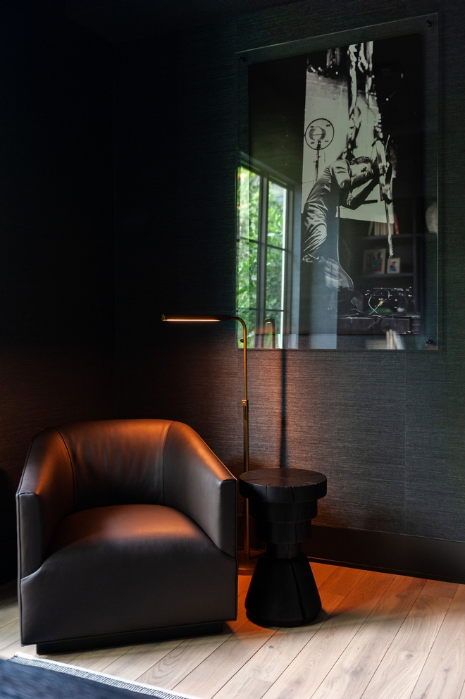 A dark and moody office space designed with a textured charcoal wallpaper displaying the homeowner’s personal photography and a leather barrel swivel chair