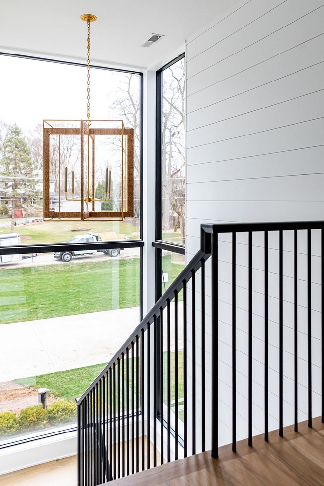 Modern Farmhouse staircase with white shiplap walls in matte white paint color large black windows and black metal stair railing and thin black metal spindles #ModernFarmhouse #staircase #whiteshiplap #shiplap #mattewhite #mattepaintcolor #largeblackwindows #blackmetalstair #blackrailing #thinspindles #blackmetalspindles