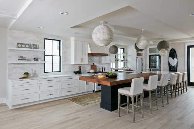 The varying pendant sizes add a playful element to the kitchen which also features an expansive island topped with a walnut counter that doubles as a dining table #kitchen #pendants #eatinisland #kitchendesign