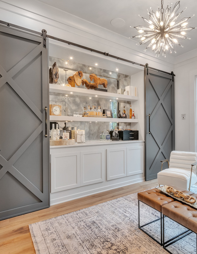 Barn doors conceal a bar with antique mirror backsplash and floating shelves #barndoor #bar #backsplash #antiquemirror #barshelves #floatingshelves