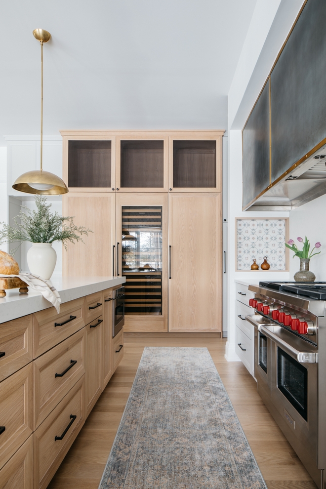 In this kitchen, White Oak cabinets and grey cabinets are accentuated with matte black hardware while a hood nook features a wall niche framed with White Oak trim and a beautiful patterned tile #kitchen #WhiteOakcabinet #greycabinet #matteblackhardware #hoodnook #wallniche #patternedtile