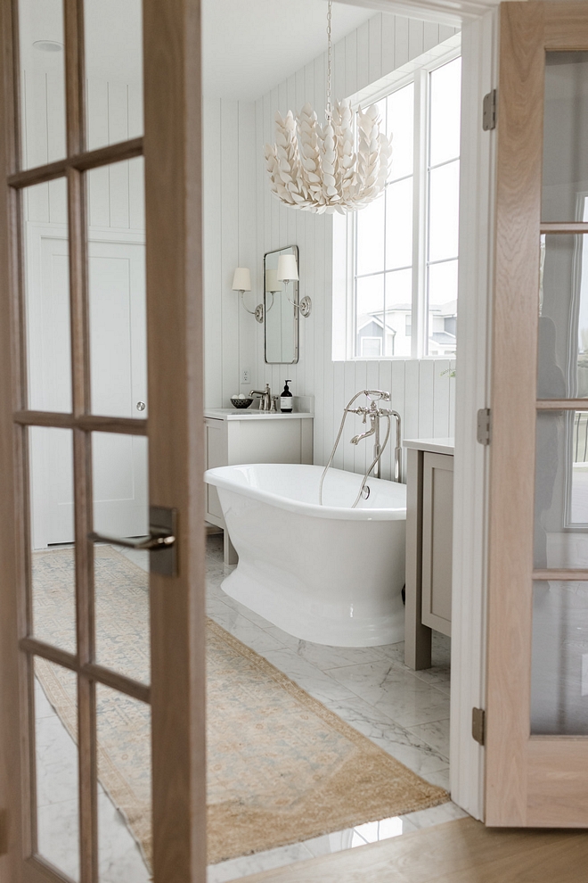 Custom White Oak French doors open into a luxurious Primary Bathroom with a cast iron pedestal tub #WhiteOakFrenchdoors #Frenchdoors #luxuriousbathroom #PrimaryBathroom #Bathroom #castirontub #pedestaltub #customvanities