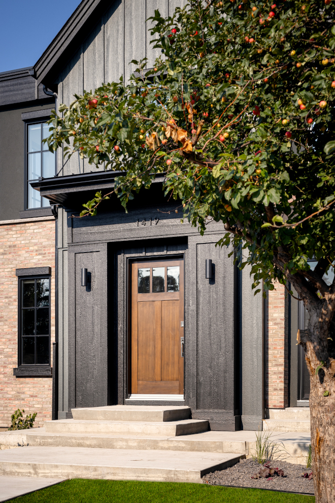 A classic Craftsman-style wooden front door beautifully complements the exterior of this home with black siding #Craftsmanstyle #frontdoor #exterior #home #blacksiding #woodfrontdoor