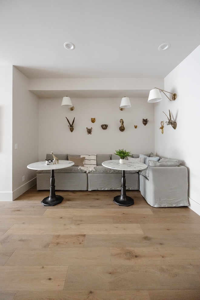 A slipcovered modular banquette paired with marble-topped tables featuring black metal bases creates a cozy atmosphere providing a relaxed versatility to this welcoming basement landing area