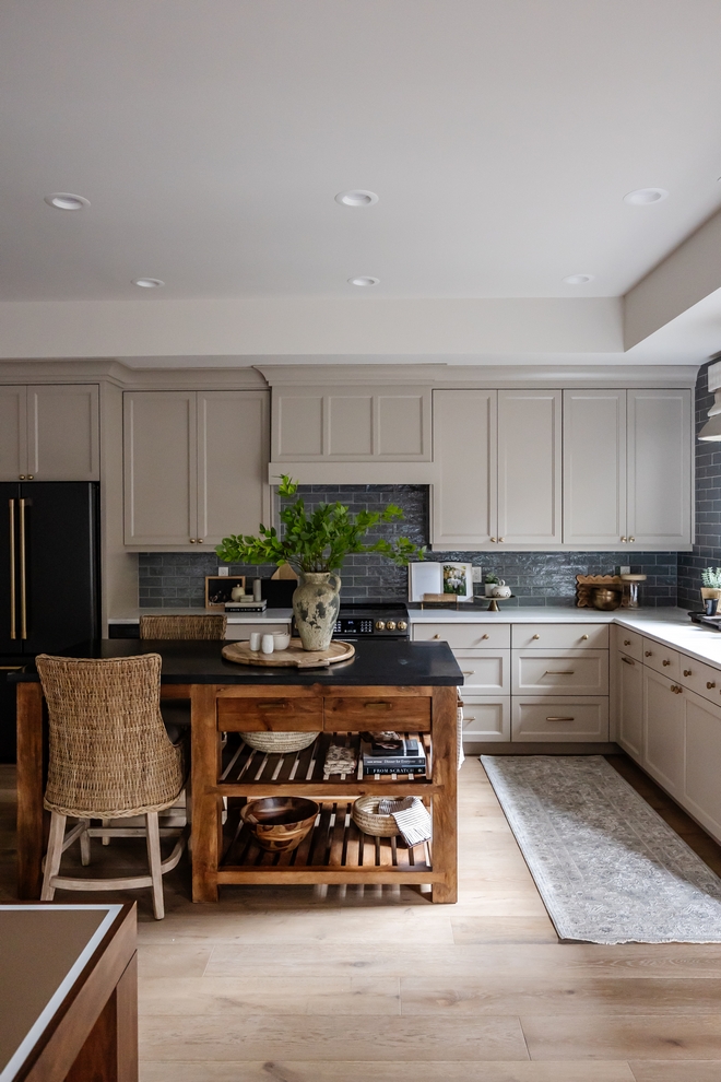 This kitchen is absolutely stunning The warm gray cabinets are beautifully complemented by a textured backsplash tile while a store-bought kitchen island adds both extra warmth and functionality