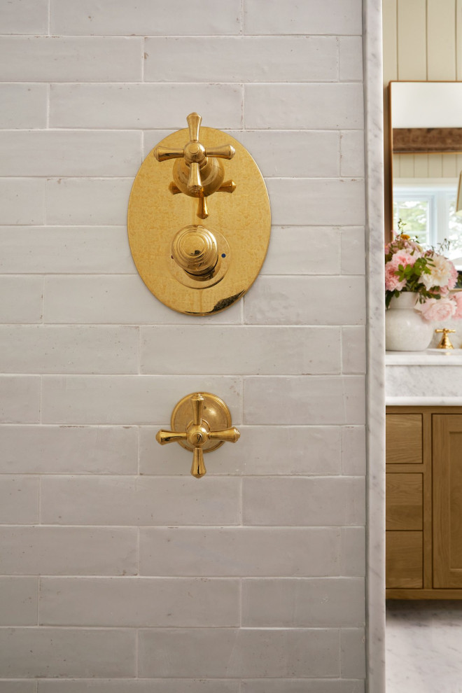 Shower wall with creamy white Italian tile and unlacquered brass fixtures in French country bathroom.