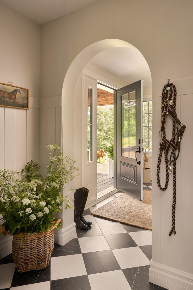 French country foyer with black-and-white marble checkered floor, warm soft white walls, braided jute rug, and arched entry to the rest of the home.