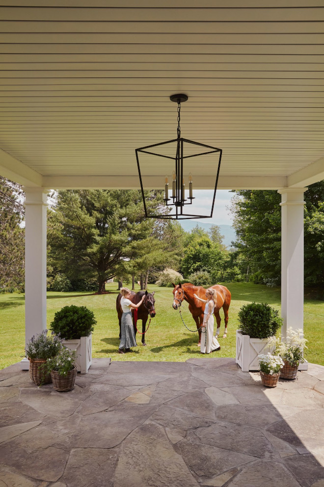 Back porch of French country home with flagstone patio, white planters, horses, mountain views, and lush greenery in Quebec.